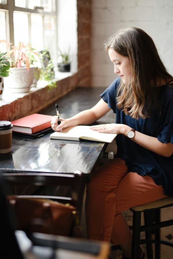 A person writes in a journal beside a bright window